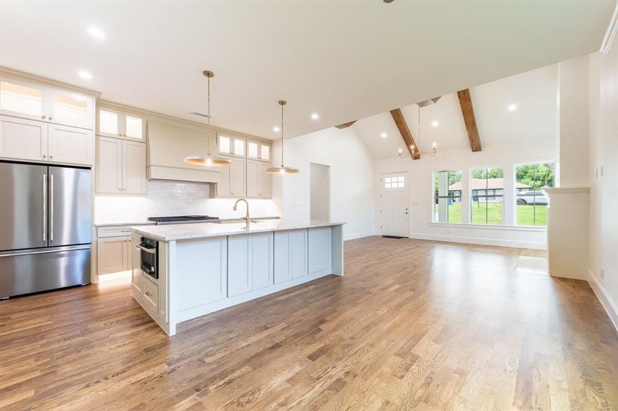 Open-concept living space with a vaulted ceiling featuring exposed wood beams, wood-finish flooring, a kitchen island with built-in microwave, and stainless steel appliances Open-concept living space with a vaulted ceiling featuring exposed wood beams, wood-finish flooring, a kitchen island with built-in microwave, and stainless steel appliances