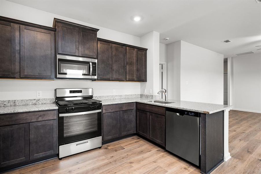 Kitchen featuring stainless steel appliances, light wood-style flooring, dark brown cabinets, light stone counters, and a peninsula