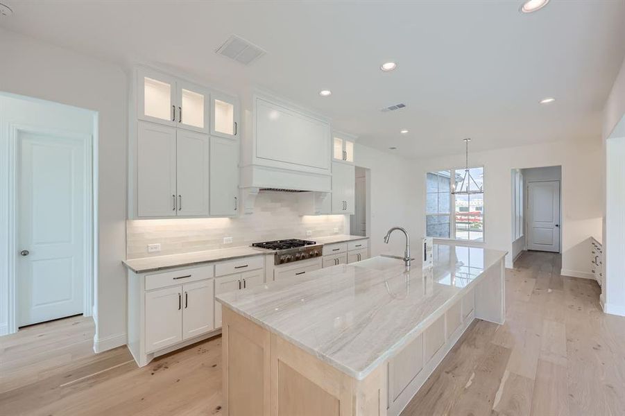 Kitchen featuring sink, white cabinets, stainless steel gas cooktop, and light wood-type flooring