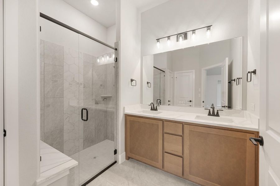 Bathroom with double sink vanity, wood cabinets, and glass-enclosed shower with hexagon tile walls Bathroom with double sink vanity, wood cabinets, and glass-enclosed shower with hexagon tile walls