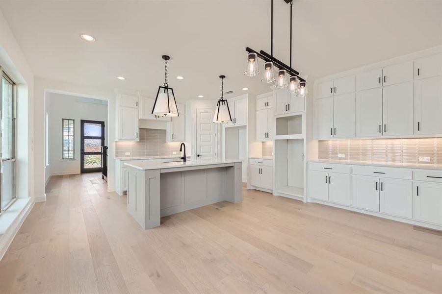 Kitchen featuring light hardwood / wood-style floors, decorative backsplash, white cabinetry, sink, and a kitchen island with sink