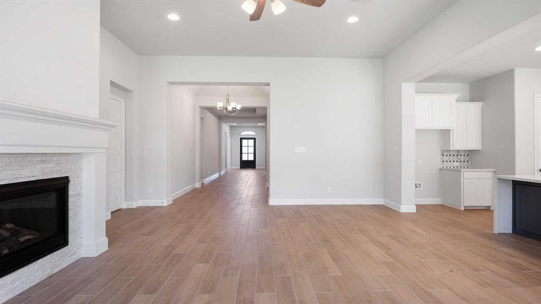 Unfurnished living room featuring ceiling fan with notable chandelier and light hardwood / wood-style floors