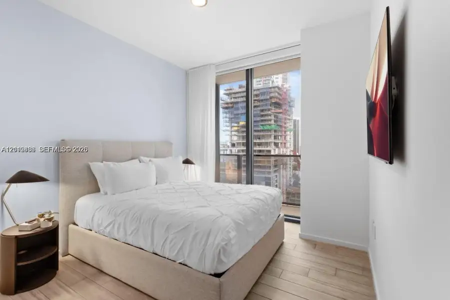 Floor-to-ceiling windows with access to a balcony, wood-finish flooring, and wall-mounted television hardware Floor-to-ceiling windows with access to a balcony, wood-finish flooring, and wall-mounted television hardware