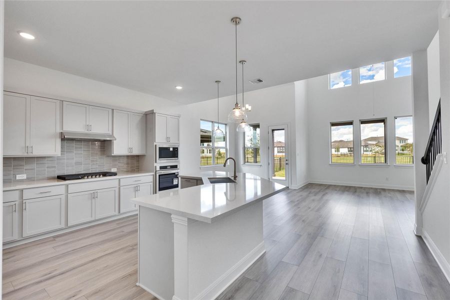 Kitchen with decorative backsplash, decorative light fixtures, light wood-style floors, an island with sink, and appliances with stainless steel finishes Kitchen with decorative backsplash, decorative light fixtures, light wood-style floors, an island with sink, and appliances with stainless steel finishes