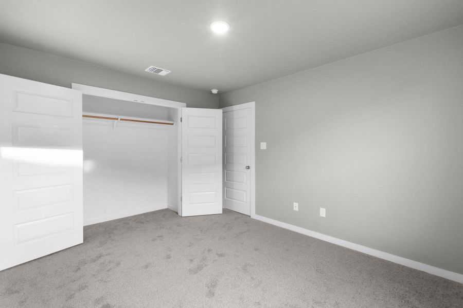 A well-lit bedroom featuring a spacious closet and neutral carpeting, ready for personalization.