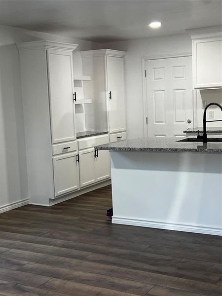 Kitchen with dark stone countertops, dark hardwood / wood-style flooring, and white cabinetry