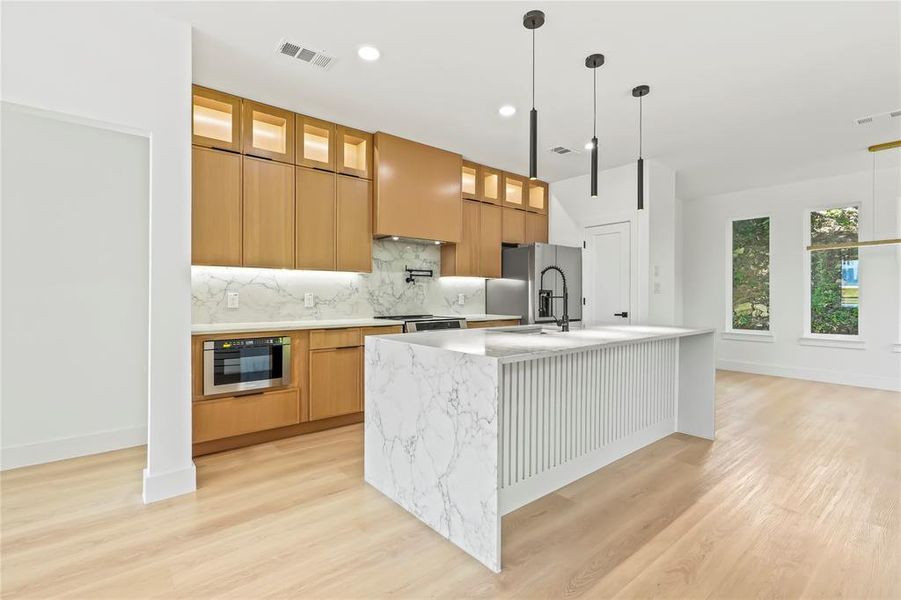 Kitchen featuring glass insert cabinets, light stone counters, a center island with sink, light wood-type flooring, and recessed lighting