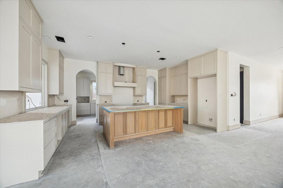 KITCHEN - Soft neutral cabinetry rises to the ceiling, creating a clean, cohesive backdrop for the space, while a warm wood island adds contrast and scale at the center. Arched openings, generous storage, and thoughtful layout details highlight a kitchen designed for both daily use and elevated entertaining. -- Construction as of 1/5/26