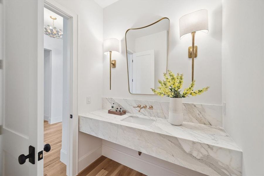 The powder room dazzles with a floating vanity, brass fixtures, decorative mirror and two light sconces.