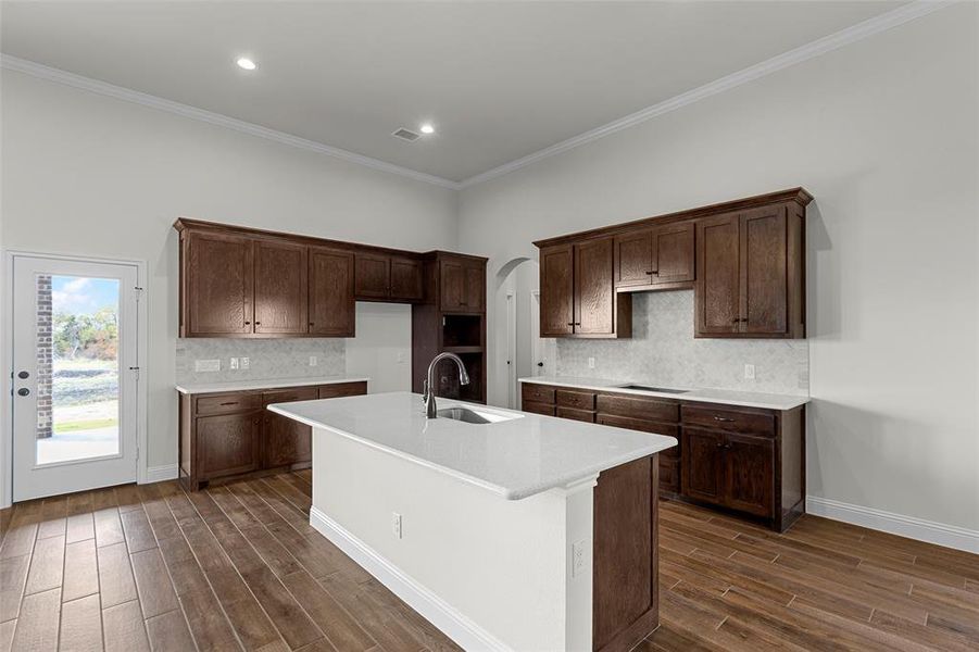 Kitchen featuring sink, cooktop, crown molding, a kitchen island with sink, and dark brown cabinets