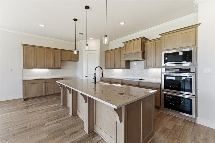 Kitchen with wood finish cabinets, a kitchen breakfast bar, a kitchen island with sink, stainless steel appliances, and ornamental molding