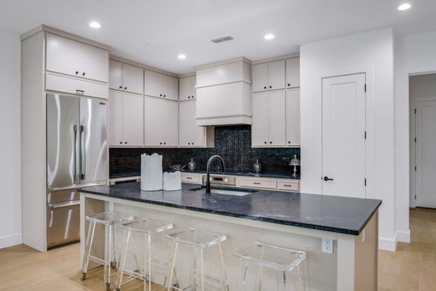 Kitchen with high quality fridge, backsplash, a sink, light wood finished floors, and dark stone countertops