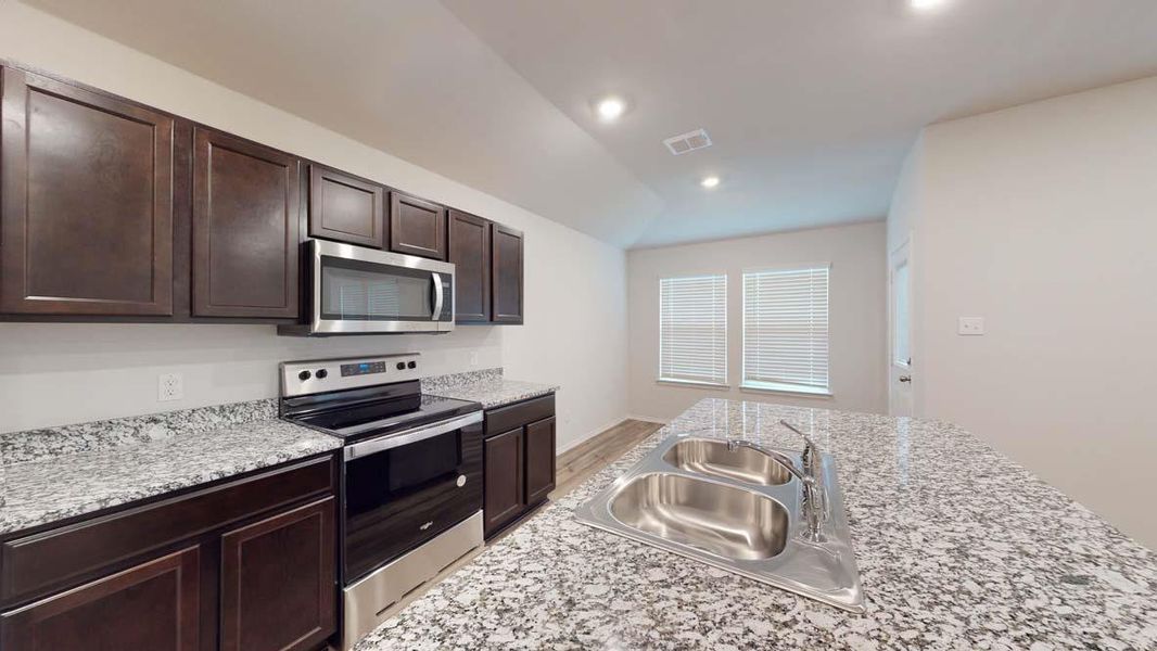 Kitchen featuring dark wood cabinetry, granite countertops, stainless steel appliances, and a double basin sink
