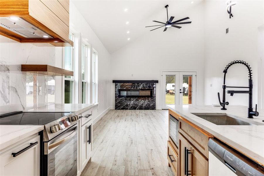 Kitchen featuring light stone counters, healthy amount of natural light, stainless steel appliances, open shelves, and high vaulted ceiling Kitchen featuring light stone counters, healthy amount of natural light, stainless steel appliances, open shelves, and high vaulted ceiling