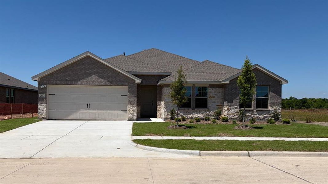 Front exterior featuring a brick and stone facade, a two-car garage, a concrete driveway, a sidewalk, and a manicured lawn with plantings