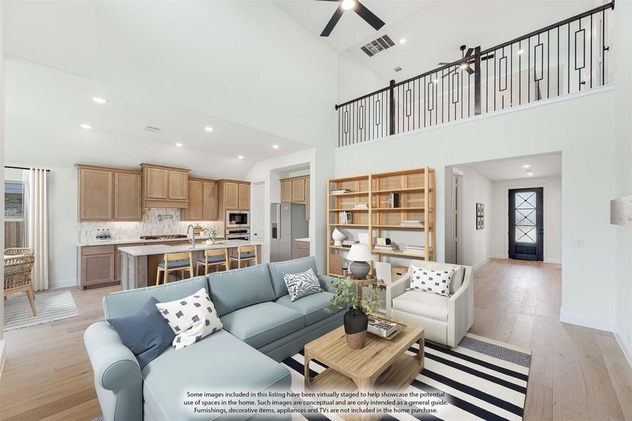 Open-concept living room with high ceilings, second-floor balcony, and kitchen visible in background with wood cabinets