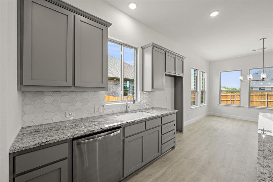 Kitchen with stainless steel dishwasher, gray cabinets, decorative backsplash, light stone counters, and recessed lighting Kitchen with stainless steel dishwasher, gray cabinets, decorative backsplash, light stone counters, and recessed lighting