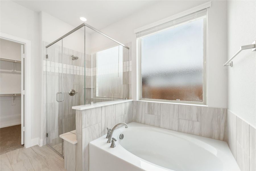 Master bathroom with soaking tub, glass-enclosed shower, tile surround, and walk-in closet entry Master bathroom with soaking tub, glass-enclosed shower, tile surround, and walk-in closet entry