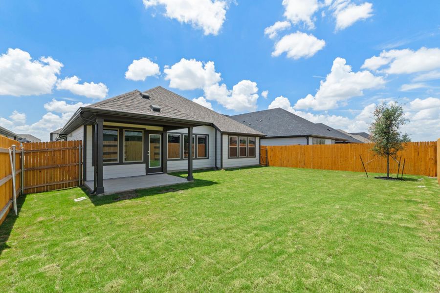 A spacious backyard with vibrant green grass, a covered patio, and a newly planted tree.