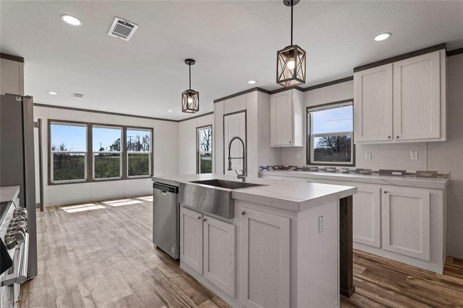 Kitchen with light countertops, an island with sink, hanging light fixtures, light wood-style floors, and crown molding
