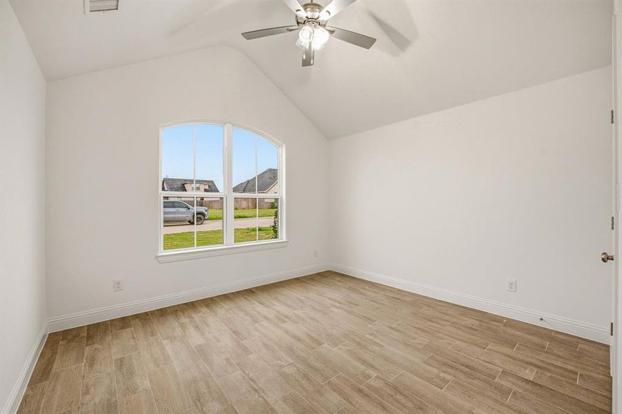 This room features a vaulted ceiling, an arched window, and wood-look tile flooring