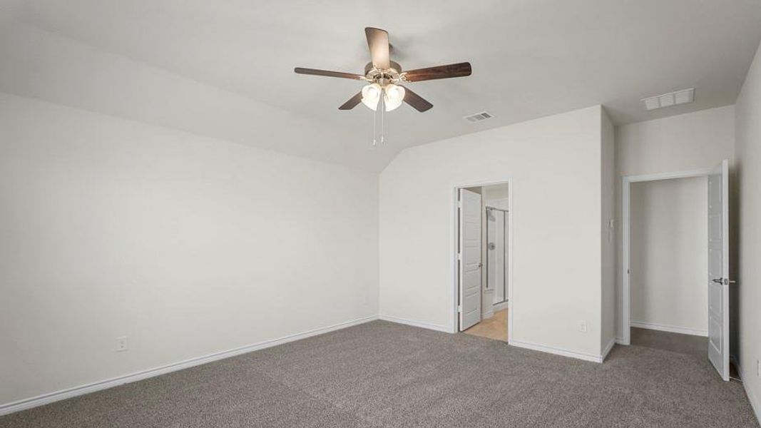 This spacious room features neutral-toned carpet flooring, a ceiling fan with integrated lighting, and white walls