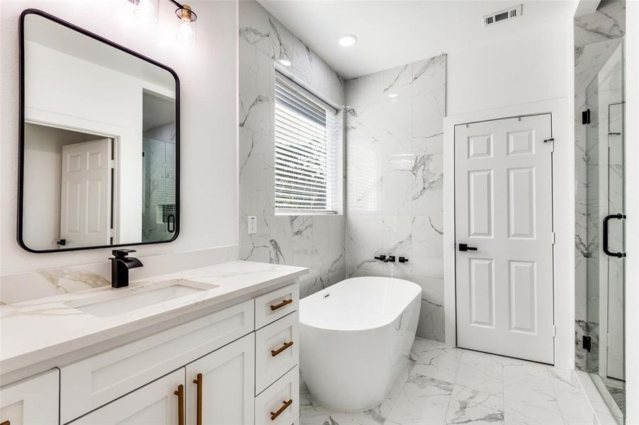 Full bath featuring light marble finish floors, vanity, a freestanding tub, a marble finish shower, and stone wall