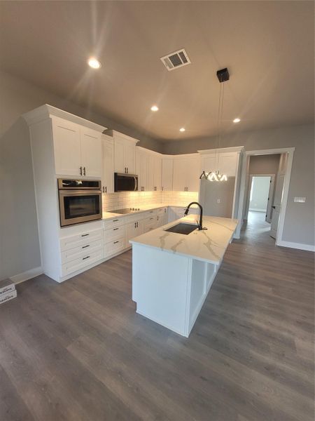 Kitchen featuring white cabinets, appliances with stainless steel finishes, decorative backsplash, a center island with sink, and light stone counters