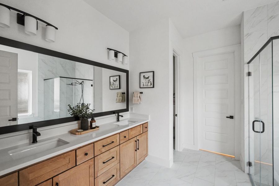 Luxurious spa-style bathroom featuring a dual-sink quartz vanity, oversized framed mirror, and sleek matte black fixtures. The glass-enclosed shower and marble-look flooring add a sophisticated, modern touch, creating a bright and refined retreat.