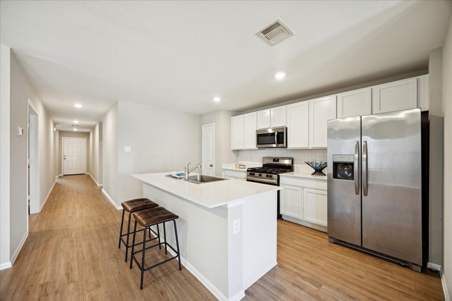 A spacious center island with bar seating, views the open layout and flows into a long entryway, creating a bright and inviting atmosphere.