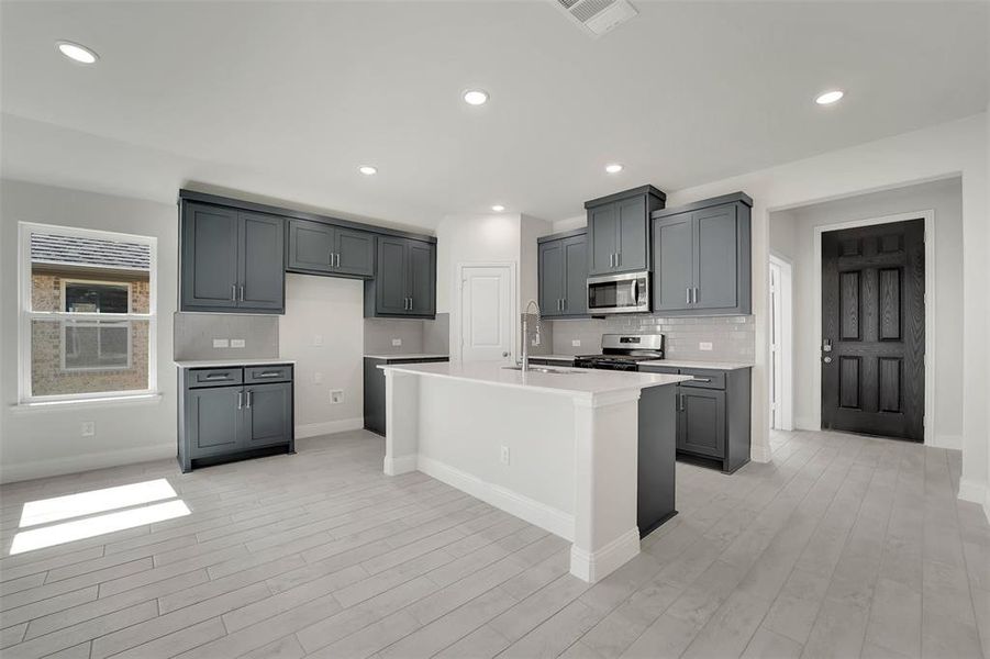 Kitchen featuring light countertops, visible vents, backsplash, appliances with stainless steel finishes, and a sink