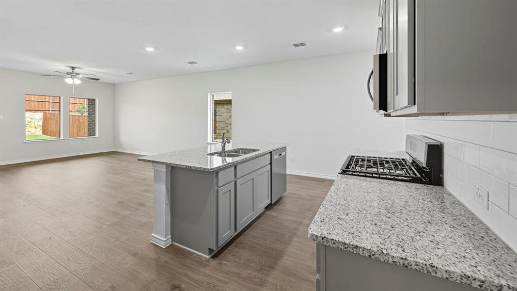 Kitchen with gray cabinets, light stone counters, stainless steel appliances, recessed lighting, and a center island with sink