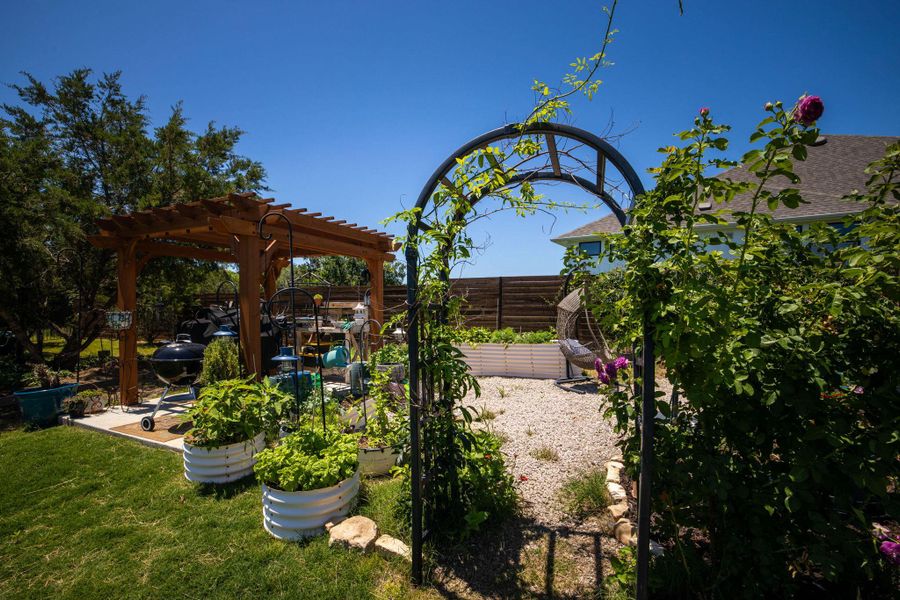 An inviting backyard haven boasts a charming wooden pergola and a delightful garden with raised beds.