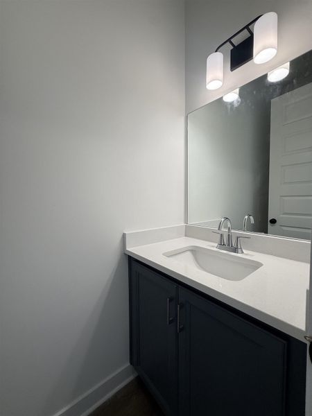 Modern vanity featuring a white countertop with integrated sink, dark cabinetry with bar pulls, chrome faucet, and contemporary wall-mounted lighting