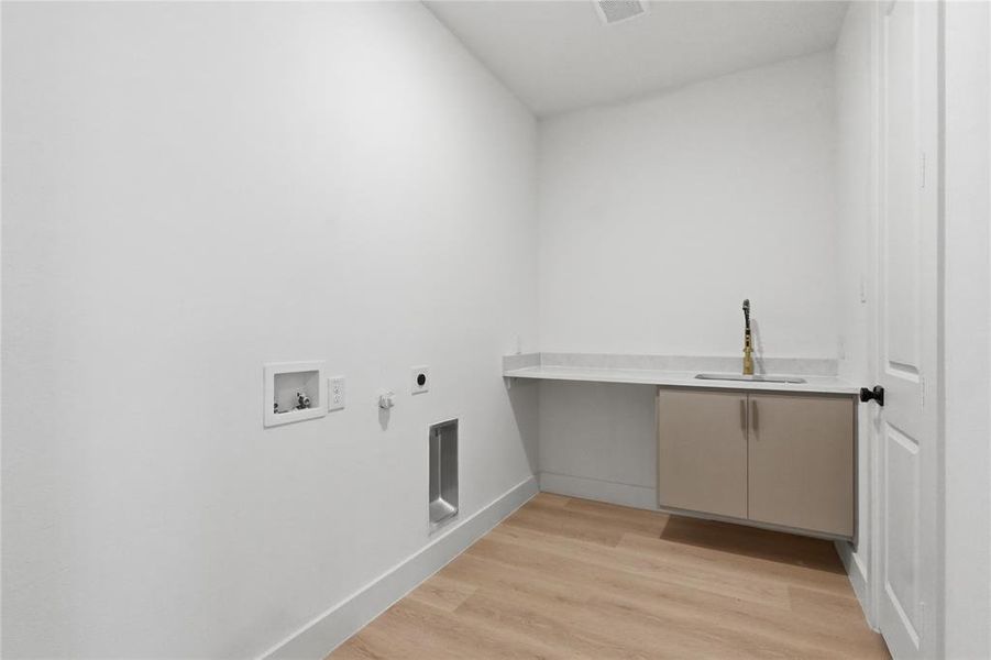 Dedicated laundry area featuring wood-finish flooring, a built-in countertop, a sink with a gold-finish faucet, and integrated cabinetry Dedicated laundry area featuring wood-finish flooring, a built-in countertop, a sink with a gold-finish faucet, and integrated cabinetry