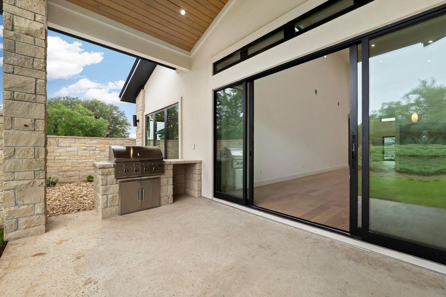 Covered patio with an integrated outdoor grill station, stone column, and wood-finish ceiling