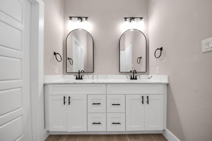 Master Bathroom with modern double vanity with sleek black fixtures, arched mirrors, and elegant lighting. The white cabinets and marble countertop offer a clean, stylish look. Master Bathroom with modern double vanity with sleek black fixtures, arched mirrors, and elegant lighting. The white cabinets and marble countertop offer a clean, stylish look.
