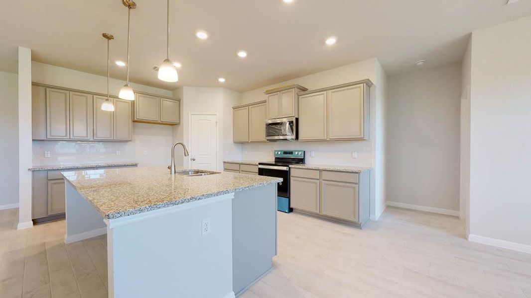 Kitchen featuring appliances with stainless steel finishes, hanging light fixtures, light stone countertops, a center island with sink, and light wood-style floors