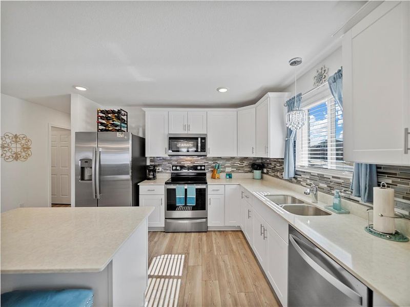 Kitchen featuring hanging light fixtures, stainless steel appliances, light countertops, white cabinetry, and a sink