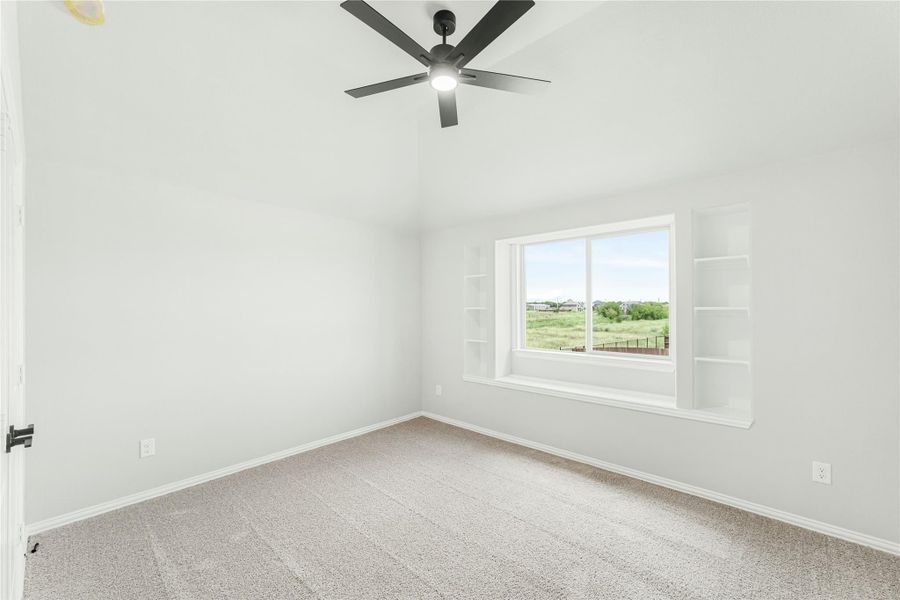 Empty bedroom with carpet, ceiling fan, large window, and built-in shelves on each side Empty bedroom with carpet, ceiling fan, large window, and built-in shelves on each side