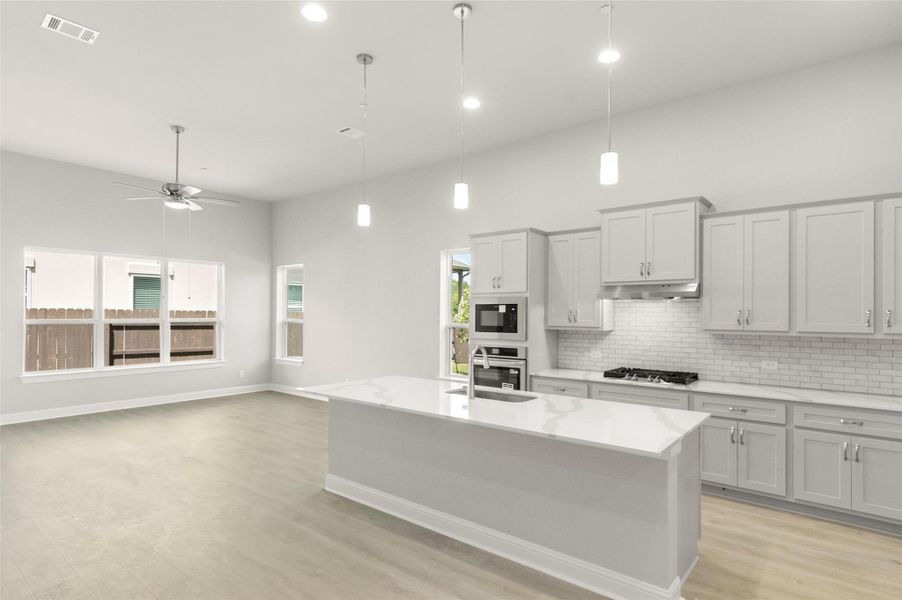 Kitchen featuring light wood-style floors, tasteful backsplash, ceiling fan, pendant lighting, and stainless steel appliances Kitchen featuring light wood-style floors, tasteful backsplash, ceiling fan, pendant lighting, and stainless steel appliances
