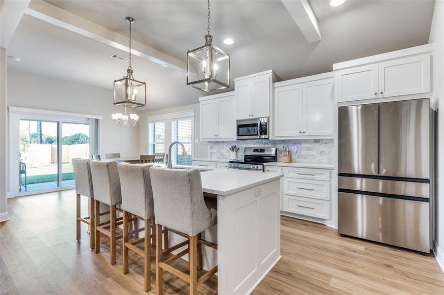 Kitchen with stainless steel appliances, decorative backsplash, pendant lighting, white cabinets, and light wood-style floors Kitchen with stainless steel appliances, decorative backsplash, pendant lighting, white cabinets, and light wood-style floors