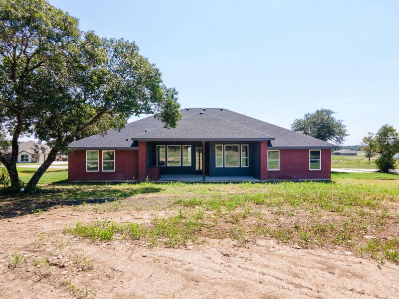 Rear view of house featuring a patio, roof with shingles, and brick siding