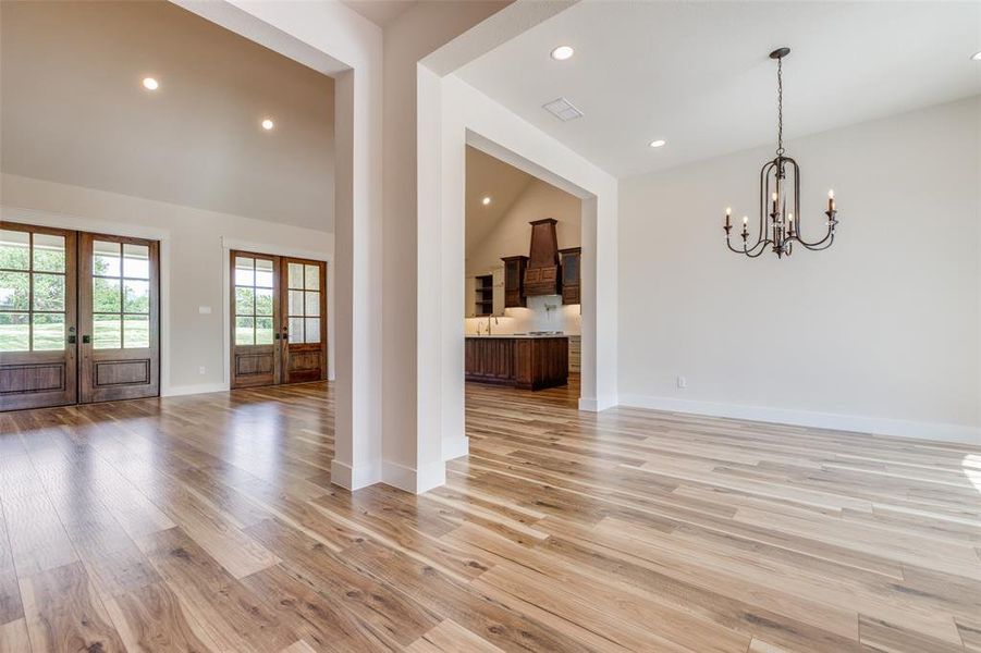 Unfurnished living room featuring light luxury vinyl wood-style floors, french doors, a chandelier, and high vaulted ceiling