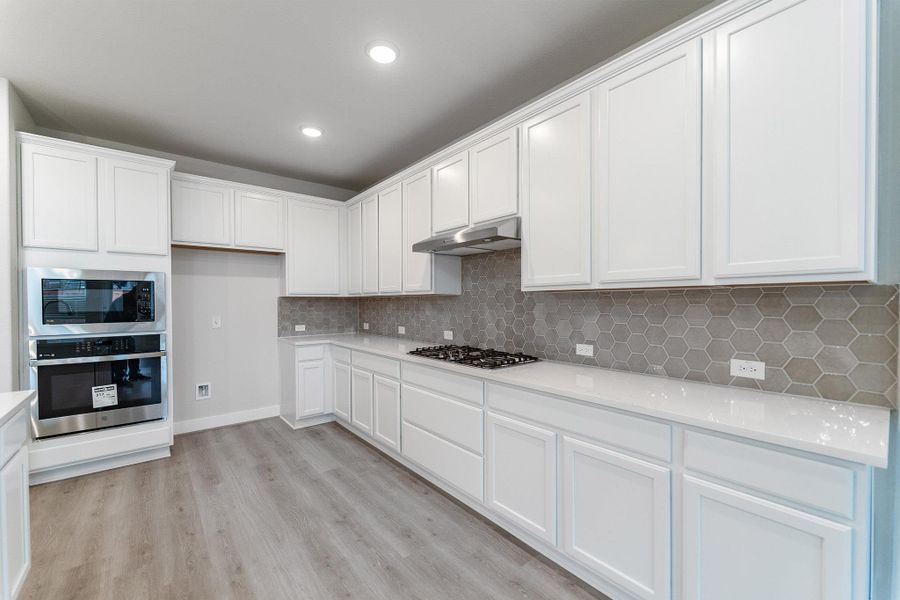 Kitchen featuring white cabinetry, stainless steel appliances, light wood-style floors, tasteful backsplash, and recessed lighting