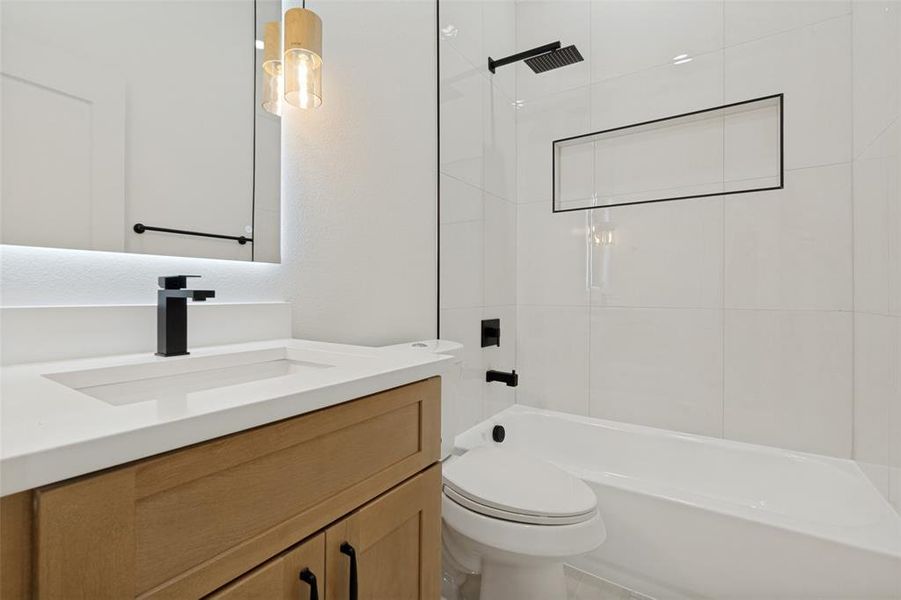 Bathroom featuring a light wood-finish vanity with an integrated sink, matte black faucet, and backlit mirror