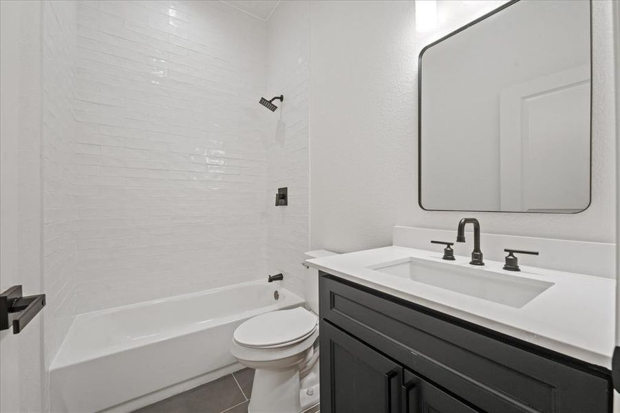Bathroom featuring a white bathtub with subway tile surround, matte black fixtures, dark wood-finish vanity with white countertop, and a rectangular mirror