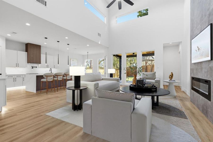 Living area featuring a fireplace, light wood finished floors, recessed lighting, a ceiling fan, and a towering ceiling Living area featuring a fireplace, light wood finished floors, recessed lighting, a ceiling fan, and a towering ceiling