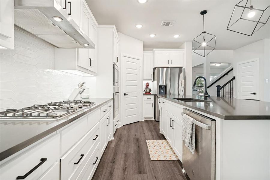 Kitchen featuring white cabinetry, dark wood-finish flooring, a stainless steel gas range, and a kitchen island with an undermount sink