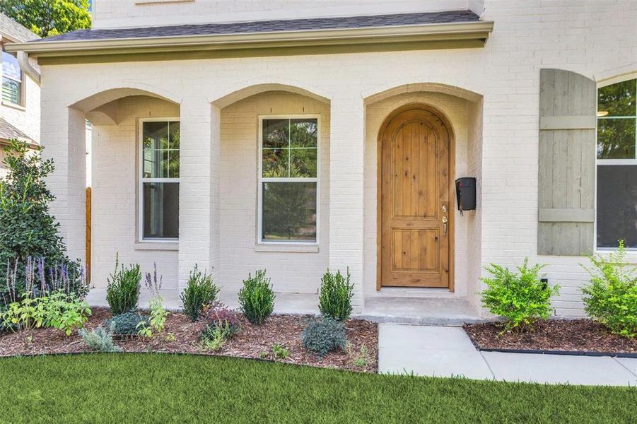 Property entrance with roof with shingles, brick siding, and covered porch